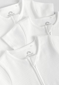 Tre hvide babyveste lavet af ribbet stof med rund halsudskæring og lynlåse. Etiketterne siger "NEXT baby."