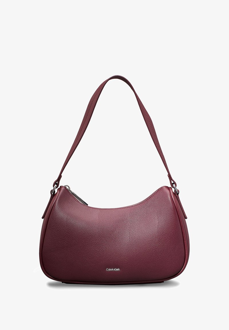 Sac d’épaule en cuir marron foncé avec forme incurvée, une seule bandoulière, fermeture éclair argentée et petit logo Calvin Klein au centre avant.