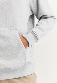Sweatshirt gris en tissu doux mélangé de coton, avec une poche frontale, des poignets côtelés et un ourlet texturé.