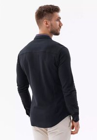 Zwarte lange mouw shirt met een kraag, voorzien van een rood en blauw gestreepte accent bij de hals, gemaakt van gladde stof, en met knoopmanchetten.