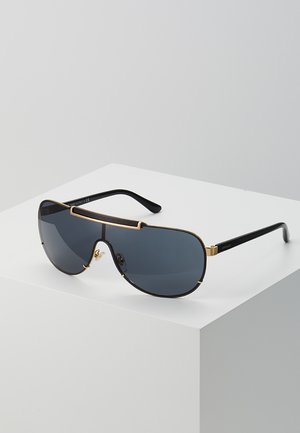 Sunglasses with large gray lenses, slim black frames, and gold accents. Features a distinctive bridge design and temple arms.