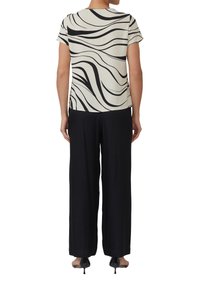 Blusa a maniche corte color crema con motivo ondulato nero, abbinata a pantaloni neri a vita alta. Tessuto liscio, vestibilità comoda e design minimal.