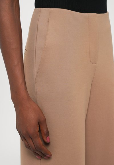 Beige stretchy bukser med en glat overflade, der har en flad foran, sidelommer og en skræddersyet pasform langs benet.