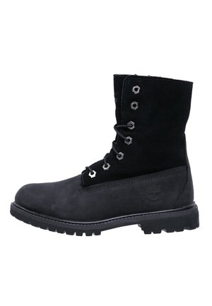 Botte cheville à lacets en cuir noir et daim, avec semelle robuste et œillets métalliques, embossée sur le côté d'un logo rond.