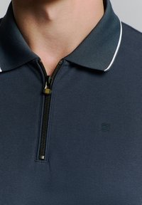 Marine poloshirt met een ritssluiting aan de voorkant. Kenmerkt zich door een gestructureerde kraag met witte accenten en een klein logodetail. Gemaakt van lichtgewicht stof.