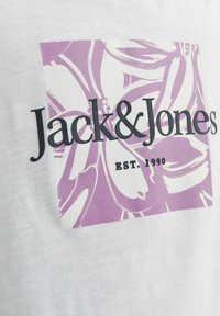 Valge T-särk, millel on lillaka mustriga ruut, kus on musta värvi rasvases kirjas "Jack & Jones" ja selle all "EST. 1990".