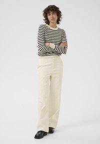 Gestreepte trui met zwarte en beige strepen, gecombineerd met crèmekleurige wijde broek. Zwarte schoenen maken de outfit compleet. Gladde textuur, casual ontwerp.