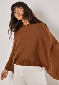 Brauner, gestrickter Pullover mit einem weiten, lockeren Design. Merkmale sind ein Rundhalsausschnitt, gerippter Saum und lange Ärmel. Kombiniert mit hellen Hosen.