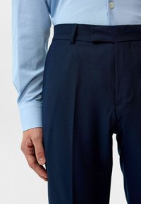 Marineblauwe broek met een gladde textuur en subtiele plooien. Draag met een lichtblauw overhemd met een knop-down kraag.