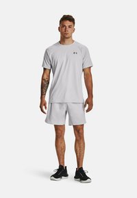 Hellgraues Sport-T-Shirt und Shorts aus atmungsaktivem Material. Mit einem kleinen schwarzen Logo auf dem Shirt, kombiniert mit schwarzen Sneakers.