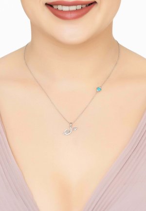 Silver necklace featuring a fish-shaped pendant with a turquoise accent and a delicate chain, worn above a v-neckline top.