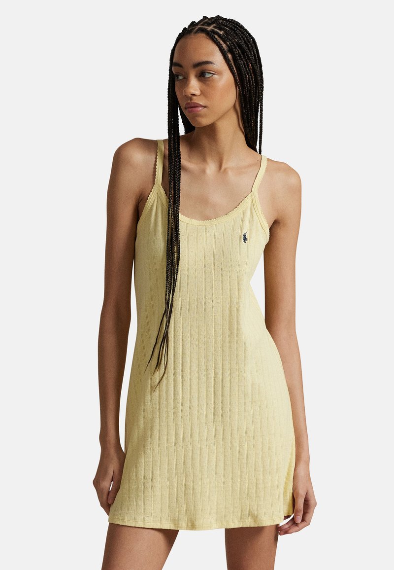 Light yellow ribbed dress with narrow straps and a rounded neckline, featuring a small logo on the chest and side slits for ease of movement.