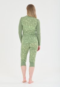 Groene loungewearset bestaande uit een langmouwtop en cropped broeken met een herhaald tekstpatroon, gemaakt van zachte stof en een aansluitend ontwerp.