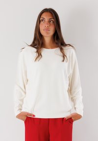Maglione bianco a maniche lunghe con collo rotondo e vestibilità rilassata, abbinato a pantaloni rossi. Presenta polsini a coste e una consistenza morbida.