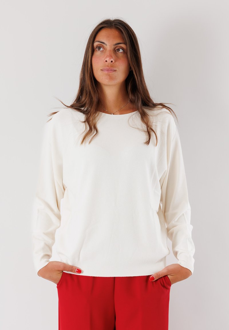 Maglione bianco a maniche lunghe con collo rotondo e vestibilità rilassata, abbinato a pantaloni rossi. Presenta polsini a coste e una consistenza morbida.