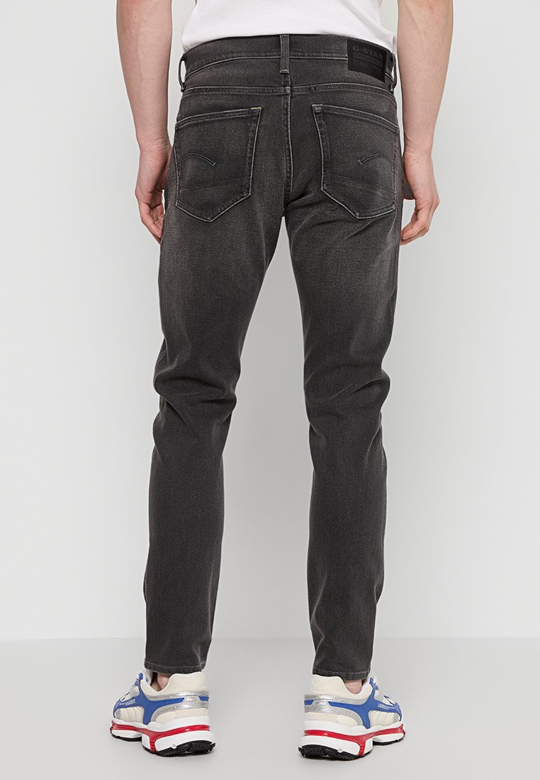 Donkergrijze denim jeans met een slim fit, voorzien van achterzakken met gestikte details. Draagt met sportieve sneakers.