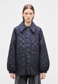 Μπλε σκούρο μπουφάν με καπιτονέ υφή, μεγάλο γιακά, κλείσιμο με κουμπιά μπροστά, δύο πλαϊνές τσέπες και ελαστικές μανσέτες. Ομαλή υφή με διαμνητό σχέδιο.