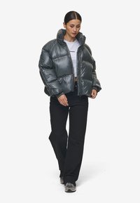 Pufferjack in metallic donkergrijs, glanzende afwerking, oversized ontwerp, taillering, gecombineerd met zwarte broek en grijze sneakers.