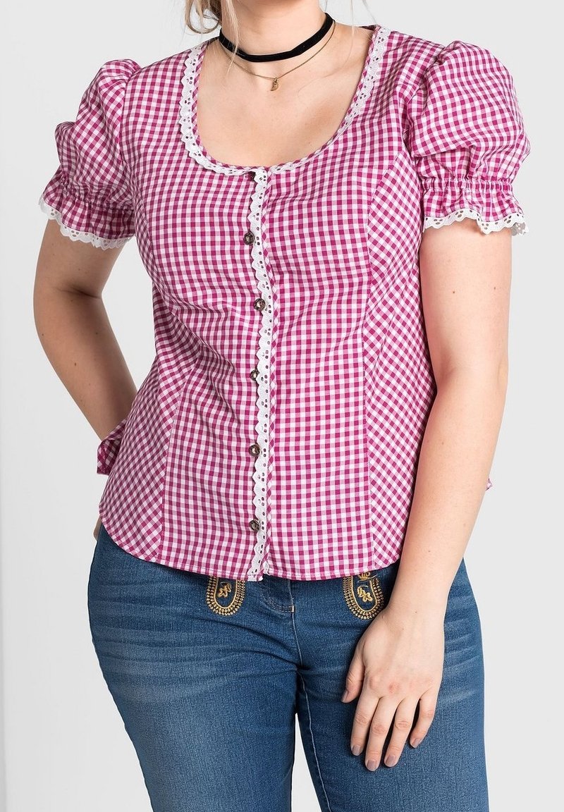 Femme portant un chemisier à carreaux rouges et blancs à boutons avec des manches bouffantes et un jean bleu avec des poches brodées.