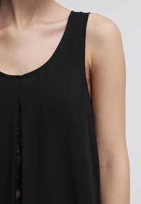 Top senza maniche nero caratterizzato da una vestibilità ampia, scollo a V e dettagli in pizzo lungo il davanti, realizzato in un tessuto leggero e liscio.