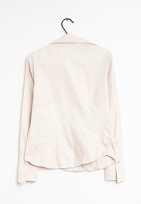 Camicia button-up di un beige chiaro, maniche lunghe, tessuto morbido, colletto strutturato, dettaglio sulla spalla posteriore e orlo curvo con polsini arrotondati.