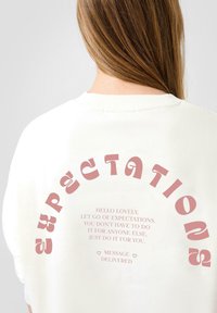 Witte sweatshirt met roze gebogen tekst op de achterkant, met een motiverende boodschap. Het stof lijkt zacht; casual ontwerp en unisex pasvorm.