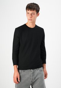 Pulover negru tricotat cu guler rotund și mâneci lungi, realizat dintr-un material moale, având un tiv ajustat și un design minimalistic.