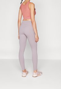 Dopasowane lawendowe legginsy i koralowy crop top z elastycznego materiału, z teksturowanym pasem u góry i jasnymi butami sportowymi.