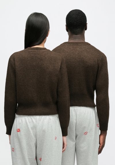 Brunstickad tröja med rund halsringning och ribbad nederkant, tillsammans med ljusgrå mjukisbyxor med röda läpptryck.