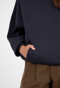 Navyblauw oversized sweatshirt met een geribbelde hals, verlaagde schouders en een voorzak. Gecombineerd met bruine textuurbroek.