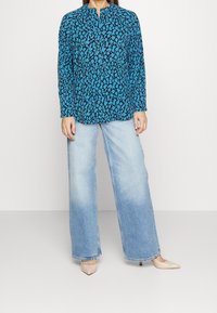 Blå og sort mønstret bluse med lange ærmer, der er parret med lyseblå brede jeans og nude spidse hæle.