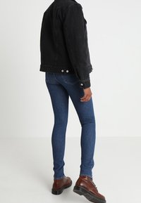 Zwarte denimjack met een klassieke snit, gecombineerd met blauwe skinny jeans. Bruine veterboots met een dikke zool. Eenvoudig en functioneel ontwerp.