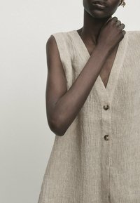 Beige Leinenkleid mit V-Ausschnitt, ärmellosem Design, aus strukturiertem Stoff und drei Knöpfen an der Vorderseite. Glatte Oberfläche, lässiger Stil.