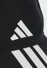 Primer plano de una tela negra con el logo blanco de Adidas y tres franjas diagonales blancas en ropa deportiva.