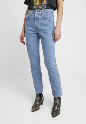 Jean en denim bleu clair avec une taille haute, coupe droite, et ourlet effiloché. Associé à des bottines noires et argentées au motif serpent.