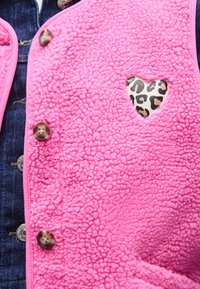 Γιλέκο από φλις σε έντονο ροζ χρώμα, με υφή στην επιφάνεια, κουμπιά και λεπτομέρεια σε σχήμα καρδιάς με τύπωμα λεοπάρ.