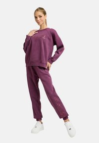 Lila Sweatshirt und passende Hose aus einem weichen Stoff, mit lockerem Schnitt, gerippten Bündchen und dezentem Branding in metallischem Pink.