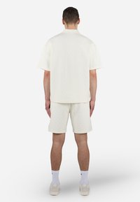 Roomwit gewatteerd shirt met korte mouwen en bijpassende korte broek, beide met een diamantpatroon, losvallend en met een zachte textuur.