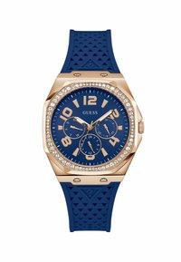 Orologio con cinturino in gomma blu e cassa in oro rosa, design ottagonale, quadrante blu, grandi numeri, tre sottodial e cristalli decorativi attorno alla lunetta.
