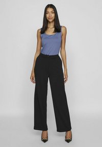 Calças largas pretas com uma cintura alta e fecho de botão, combinadas com uma blusa justa azul e sapatos de salto agudo pretos.