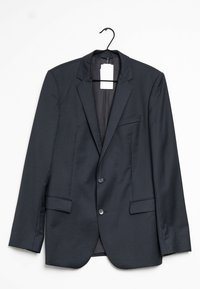 Blazer nero a righe, con rever a punta, due tasche anteriori e due bottoni. Sospeso a un gancio nero, etichetta visibile all'interno.