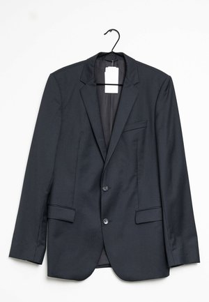 Mustapilkullinen bleiseri, jossa on läpivärjätty kaulus, kaksi etutaskua ja kaksi nappia. Roikkuu mustassa koukussa, tunnus näkyvissä sisällä.