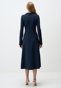 Robe bleu marine à manches longues avec un col, corsage ajusté et jupe évasée. Texture lisse et longueur mi-mollet, présentant un minimum de détails.