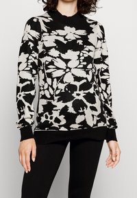 Svart och krämfärgad blommig mönstrad tröja med rund halsringning, långa ärmar och ribbade muddar, som bärs med svarta leggings.