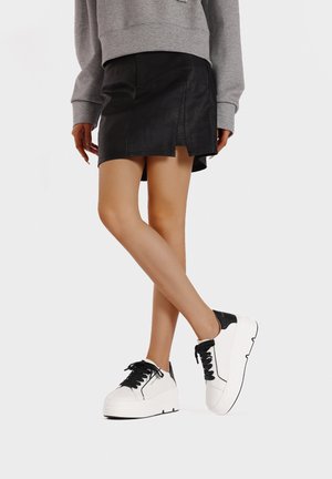 Sneakers platform bianchi con accenti neri, abbinate a una mini gonna in pelle nera con uno spacco laterale, e a una felpa grigia oversized.