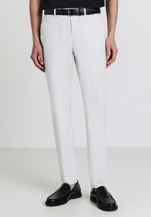 Pantaloni aderenti di colore grigio chiaro realizzati in tessuto liscio, con tasche anteriori e una cintura in pelle nera. Indossati con mocassini neri.