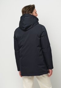 Mörkblå isolerad jacka med huva, med en slät yta och långa ärmar, sedd från baksidan.