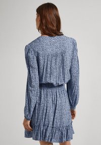 Sininen kukkamekko, jossa on pitkät hihat, smockattu vyötärö ja röyhelöhelma. Pehmeä kangas sisältää hienostuneen kuvion koko matkalta.