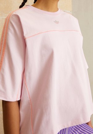 T-shirt oversize rose clair à manches courtes, avec des accents orange et un logo discret sur la poitrine. Tissu en coton doux.