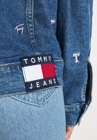 Spijkerjack met een blauwe wassing, met een groot rechthoekig Tommy Jeans-logo in marineblauw, rood en wit op de achterzak.